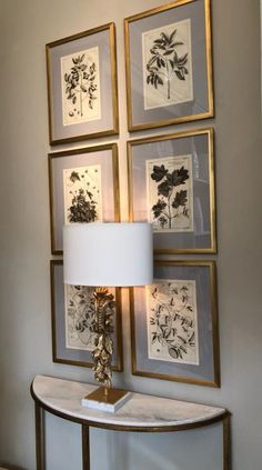 a lamp sitting on top of a white table next to framed pictures and flowers in gold frames