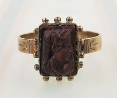 "A Tiger's eye carved cameo is centered on this antique Victorian 10k yellow gold ring. The rectangular reddish brown stone with subtle chatoyancy measures 9.5mm by 6.6mm.  The carved profile depicts a lady with long curly locks facing right. Twisted trim and dots surround the bezel. A carved design decorates the ring's shoulders. The ring was finished with a sturdy 3mm wide band. The setting tested as 10k gold purity (no hallmark). It measures a size 8 and could be re-sized by an experienced je Brown Oval Cabochon Rings, Brown Gemstone Rings In 14k Gold, Brown Oval Victorian Jewelry, Victorian Bronze Brass Ring, Antique Brown Cabochon Ring, Tigers Eye Gem, Brown Stone, Cameo Ring, Gold Art Deco