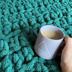 a person holding a coffee cup on top of a green blanket