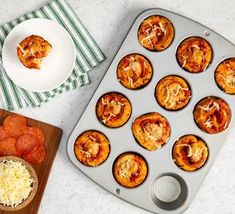 a muffin tin filled with mini pizzas on top of a counter next to a cutting board