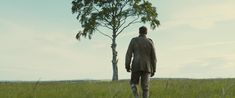 a man standing in the middle of a field next to a tree