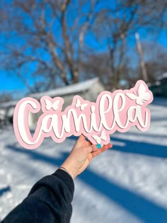 a person holding up a pink sign that says camellla in front of snow covered ground