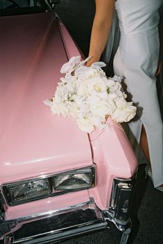 a bouquet of white flowers sits on the hood of a pink car