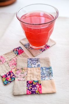 there is a glass of wine on the table next to two coasters that have patchwork designs