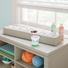 a window sill with yarn, cups and toothbrushes sitting on top of it