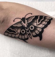 a black and white moth tattoo on the left upper arm, with an intricate design