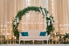 a white couch sitting under a green and white floral arch on top of a stage