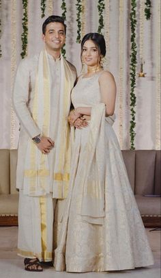 a man and woman standing next to each other in front of a wall with flowers