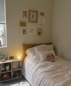 a bed with white sheets and pillows next to a book shelf filled with books in front of a window