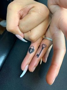 two people holding hands with tattoos on their fingers and one has a key tattoo on it