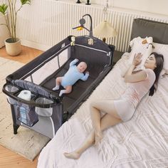 a woman laying on top of a bed next to a baby in a crib