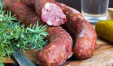 two sausages on a cutting board next to a glass of water and some herbs