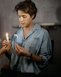 a young man holding a candle in his hands and looking at it with one hand