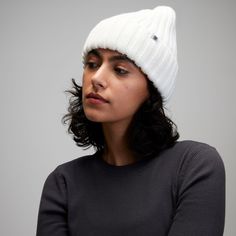 a woman wearing a white knitted beanie looks off to the side with her hand on her hip