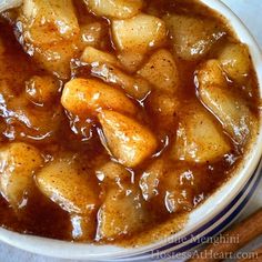 a bowl filled with stew and potatoes on top of a white table next to two wooden spoons