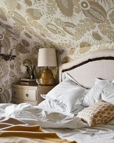 a bed with white sheets and pillows in a bedroom next to a wallpapered wall