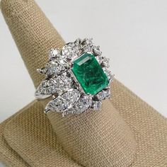 This Platinum Vintage Ring has a stunning large emerald as its center piece. The emerald has strong intense green color and shimmers as you move the piece around! The emerald is set with prongs and on all sides surrounded with sparkly high quality eye clean diamonds in flower petal shapes. There are a total of 57 round brilliants for a total of 2 carats. The ring is a size 7.5.This ring is a great collector's piece with its sparkly flowery design and good quality large emerald!Ring Size: 7.5Tota Dazzling Green Emerald Diamond Ring, Exquisite Green Emerald Platinum Ring, Luxury Green Baguette Cut Emerald Ring, Luxury Green Emerald Ring With Vvs Clarity, Exquisite Green Emerald Diamond Ring, Luxury Green Emerald Ring With Center Stone, Luxury Green Emerald Diamond Ring, Dazzling Emerald Ring In Emerald Cut, Luxury Green Emerald Ring With Brilliant Cut