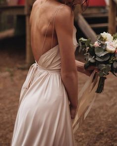 a woman in a white dress holding a bouquet and looking at the back of her dress