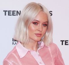 a woman with blonde hair wearing a pink shirt and diamond earrings, posing for the camera