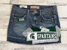 *READY TO SHIP* This ladies size 3 Michigan State University MSU themed denim patch skirt the perfect way to show support to your favorite school! I began with a size 3 gently worn Candies brand denim skirt and have sewn Michigan State University fabrics on the front & back of the skirt along with a rescued t-shirt piece to create a unique one of a kind design!  The following details & measurements will help you decide if the fit would be right for you!  *Fabric content: 98% cotton/ 2% polyester *Waist laying flat: 14" *Around the "outside" of the waistband, through the belt loops: 29.5." *Hip laying flat: 17" *Length (measured from the side): 12" The edges of the fabric pieces will intentionally fray. This gives them the desireable "vintage" fray appearance. The more the skirt is washed & Skirt With Patches, Patch Skirt, Bed Party, Jeans Patch, Rush Week, Clothing Upcycle, Patch Denim, College Fits, Michigan State University