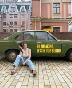 a woman sitting on the ground in front of a green car with an ad for film making it's in our blood