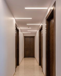 an empty hallway with wooden doors leading to another room on the other side and light above