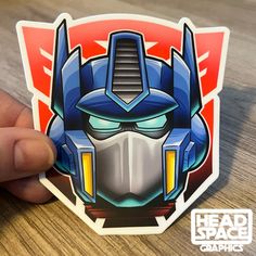 a hand holding up a sticker with the image of a robot head on it