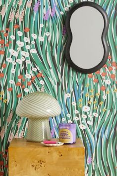 a table with a lamp and mirror next to a flowered wallpaper pattern on the wall