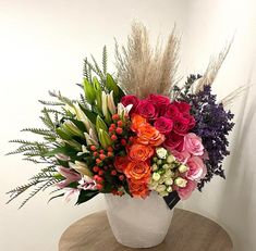 a white vase filled with lots of different colored flowers on top of a wooden table