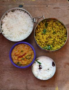 three bowls with rice, curry and other food items on a wooden table next to each other