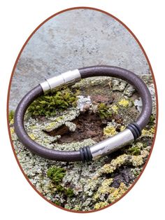 a leather and metal bracelet on top of a rock with moss growing on the rocks