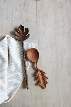 two wooden spoons sitting on top of a white towel next to an oak leaf