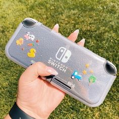 a hand holding a nintendo switch case with stickers on it's side in the grass