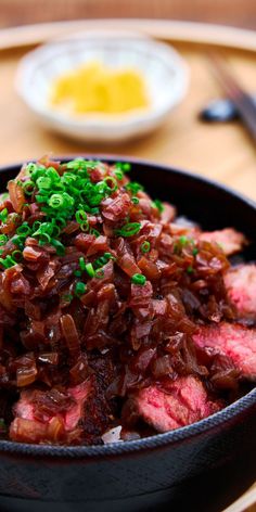 a black bowl filled with meat and green onions