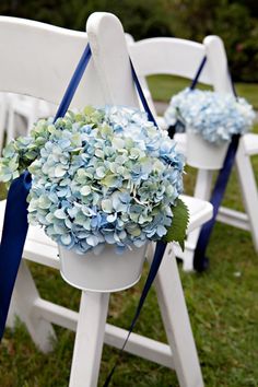 two white chairs with blue sashes and flowers in them on the grass near each other