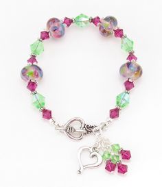 "This colorful lampwork beaded bracelet is called \"Fantasy Swirl!\" 💗 Bracelet features lovely SRA Lampwork Glass Beads by artist Sheri Chase Jones. These beads feature a lovely clear pale purple base with steaks of yellow, green, blue, purple, and fuchsia. Measures 8.5 mm x 12.5 mm. 💗 Bracelet also features Preciosa crystals in a vibrant shade of fuchsia and light green AB Czech glass beads.  💗 Beads are embellished with delicately detailed antique silver-colored spacer beads and bead caps. 💗 Bracelet is finished with an antique silver toggle closure, a heart charm, and a triple beaded charm.  💗 Bracelet measures 8 inches long. Wear this bracelet as your own piece of art, or give it as a gift to the Happy Girl in your life! Want to see more bracelets? You can find many more styles i Swirl Bracelet, Lampwork Jewelry, Pale Purple, Jewelry Summer, Green Blue Purple, Spring Jewelry, Toggle Bracelet, Lampwork Glass Beads, Bead Caps