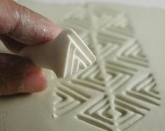 a hand holding a white object in front of a piece of paper with an intricate design on it