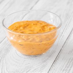 a glass bowl filled with yellow sauce on top of a white wooden table