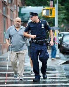 a police officer is walking across the street with an older man on a cane behind him