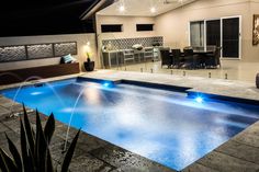 an outdoor swimming pool at night with lights on the patio and dining area in the background