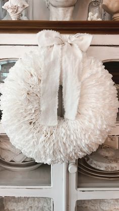 a white wreath hanging on the front door of a house with plates and dishes behind it