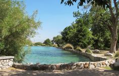 a large body of water surrounded by trees and rocks on the side of a road