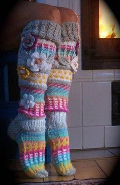 someone is wearing colorful knitted socks with flowers on the bottom, and they are standing in front of a fire place