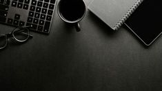 a desk with a keyboard, coffee cup and eyeglasses