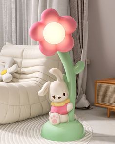 a little white rabbit sitting on top of a green plant next to a pink flower