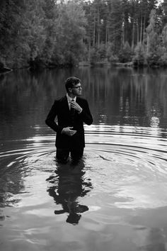 a man in a suit standing in the middle of a lake with his hands on his hips