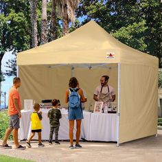 a group of people standing under a tent next to each other on a sidewalk in front of trees