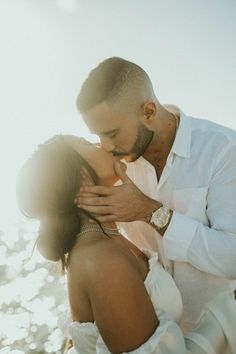 a man and woman kissing each other in front of the ocean with sunlight streaming through them