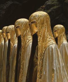 several golden cloth covered people standing next to each other in front of a rock formation