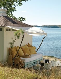 an outdoor seating area next to the water with pillows and umbrellas on it's side